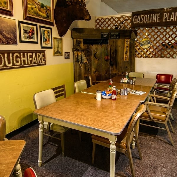 Rustic diner interior with wooden tables, chairs, and quirky wall decor including a "No Thoroughfare" sign.
