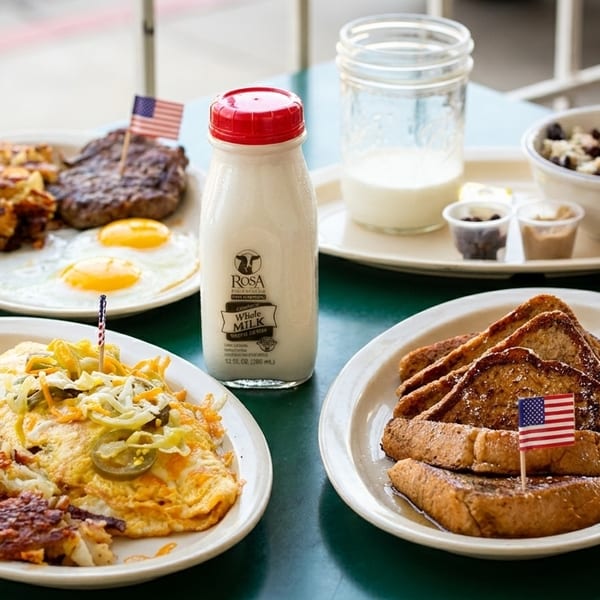 Plates of breakfast food including eggs, hash browns, sausage, French toast, and milk bottles.