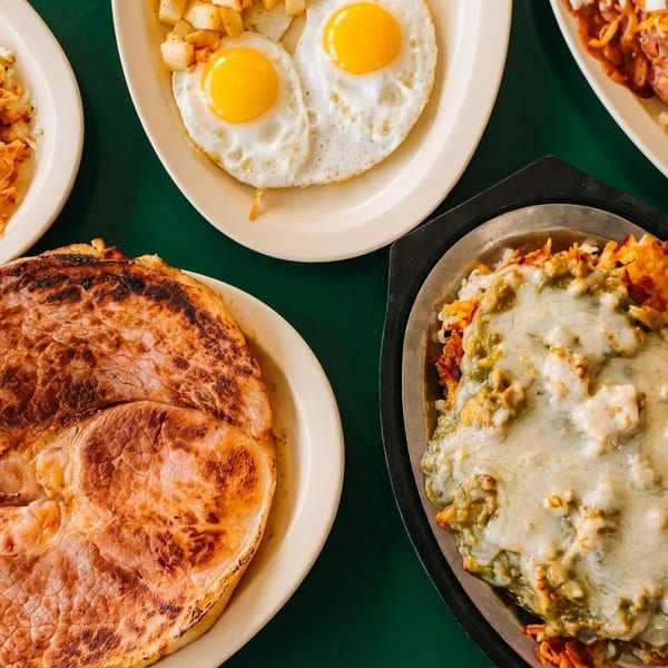 A diner spread with ham, hash browns, fried eggs, chili cheese fries, and chilaquiles.